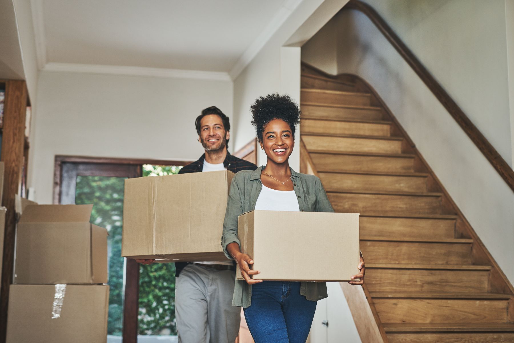 Happy couple carrying moving boxes down wooden stairs in their home