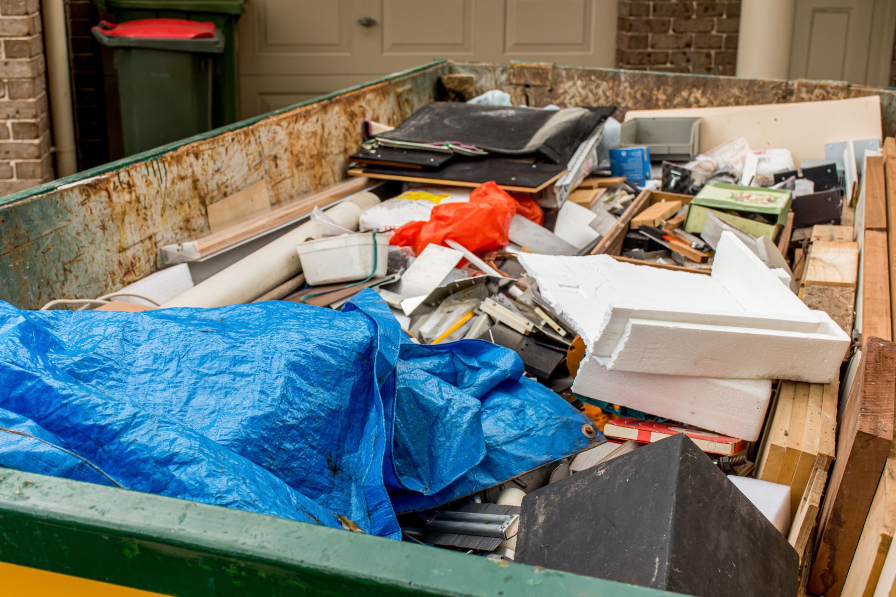 Overflowing dumpster filled with mixed waste including cardboard, metal, plastic, and debris